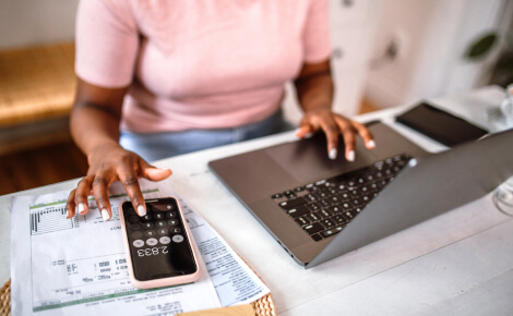woman using a laptop and a calculator app on a smartphone