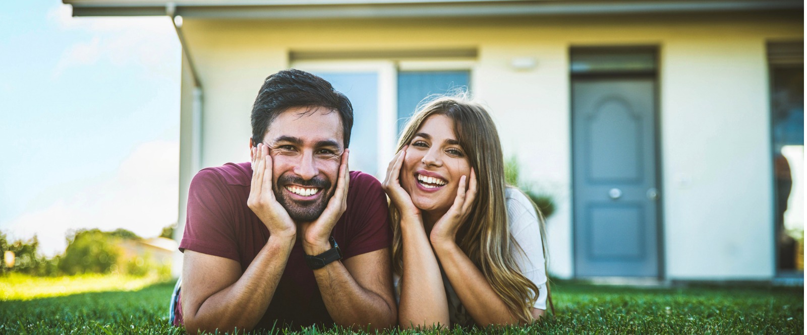 Young couple lying on the grass in front their home.